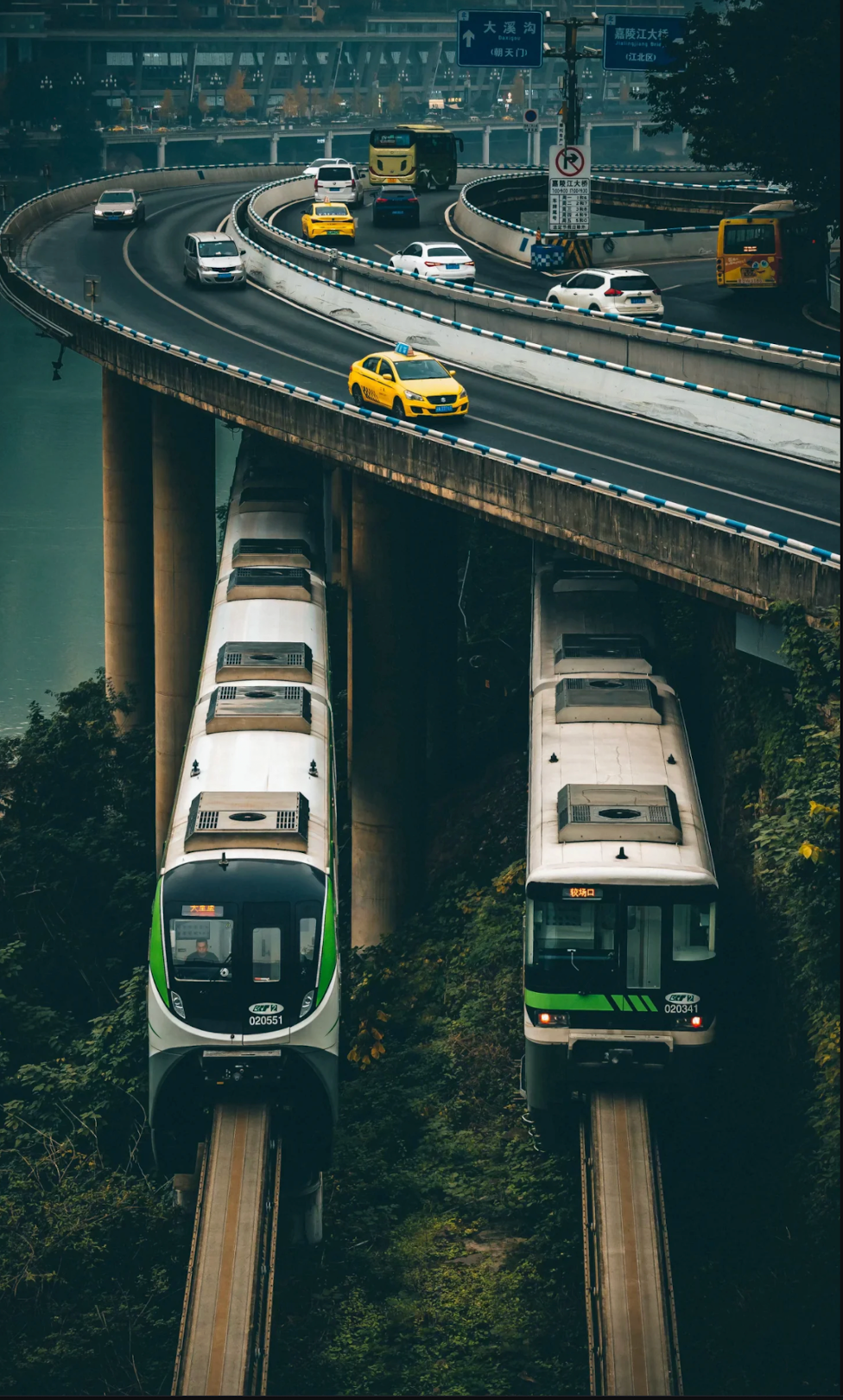 Two trains moving through Chongqing beneath layered roads